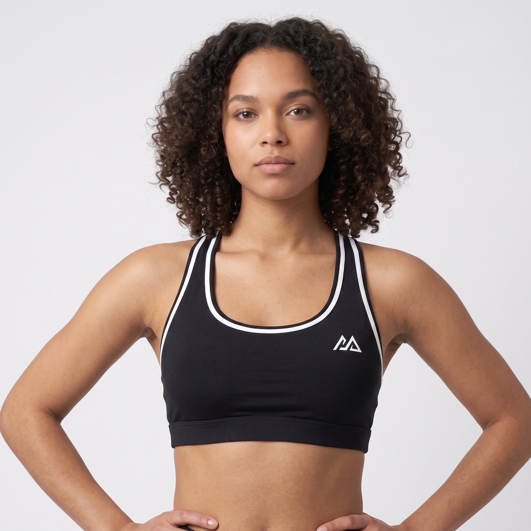 Model wearing the black Obsidian Sports Top with white trim, front view, hands on hips, Marko two-peak mark at the chest