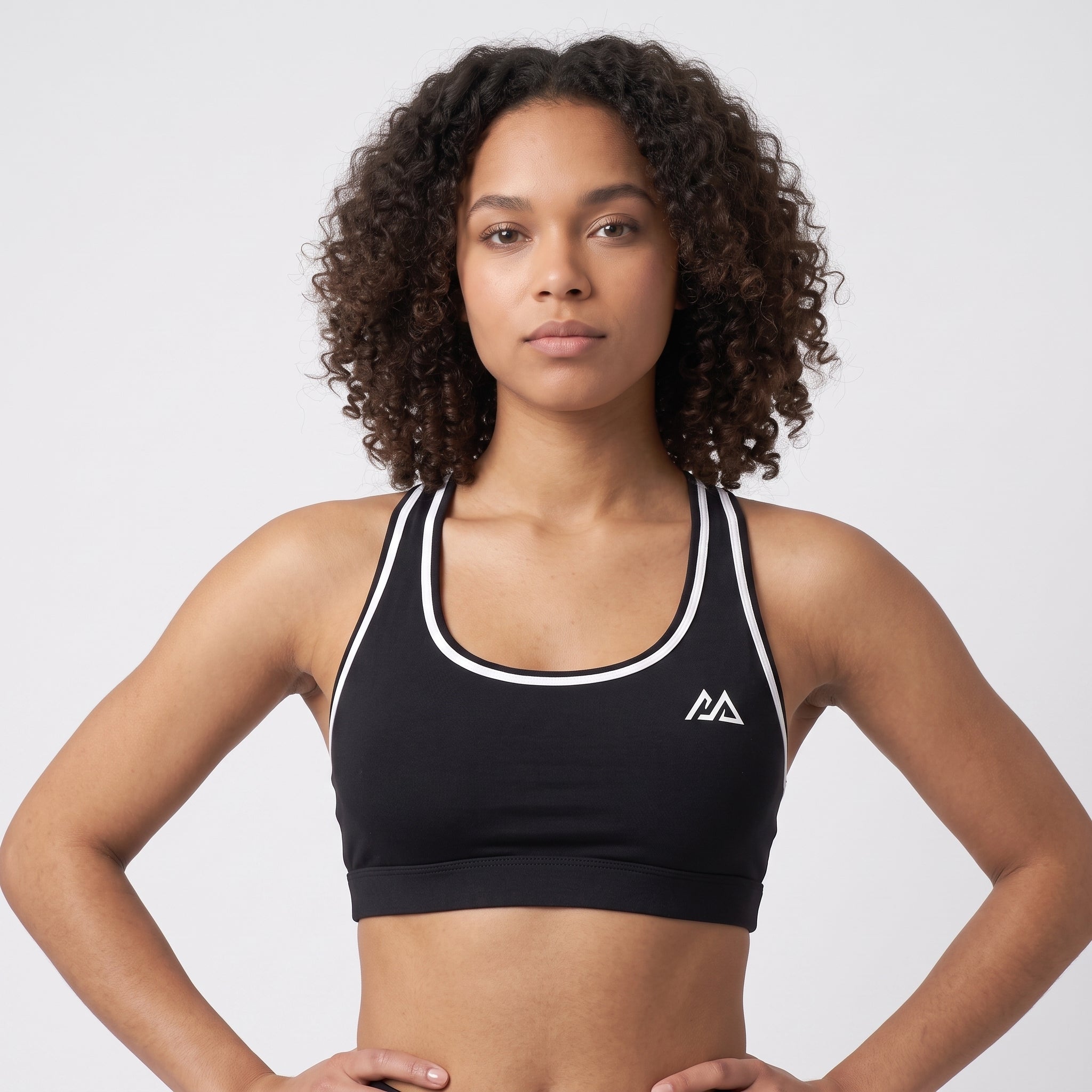 Model wearing the black Obsidian Sports Top with white trim, front view, hands on hips, Marko two-peak mark at the chest