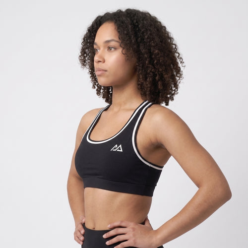 Model wearing the black Obsidian Sports Top with white trim, three-quarter view showing the racerback straps and white piping
