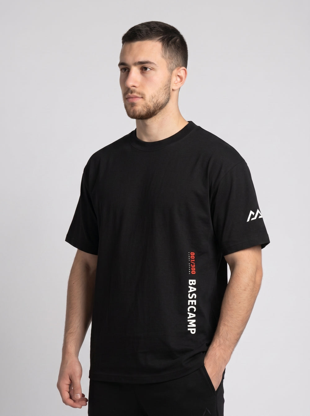 Model wearing the black 300 Heavyweight Tee, three-quarter front view, 001/300 First Ascent and BASECAMP printed vertically at the hem