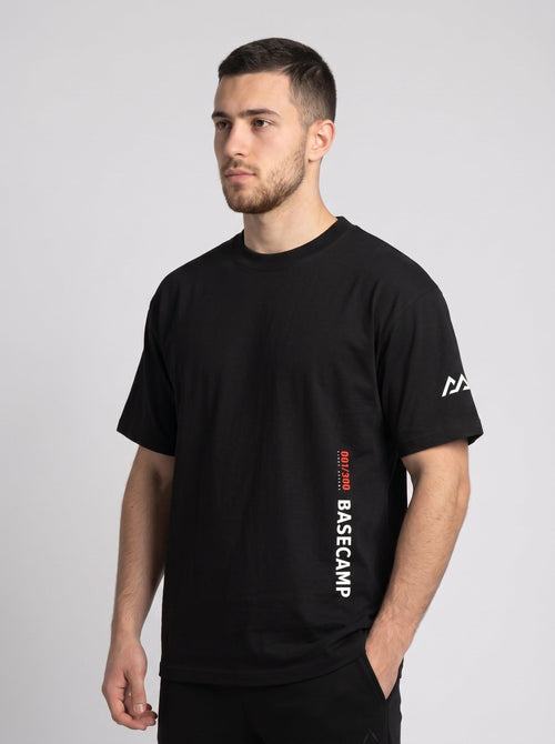 Model wearing the black 300 Heavyweight Tee, three-quarter front view, 001/300 First Ascent and BASECAMP printed vertically at the hem