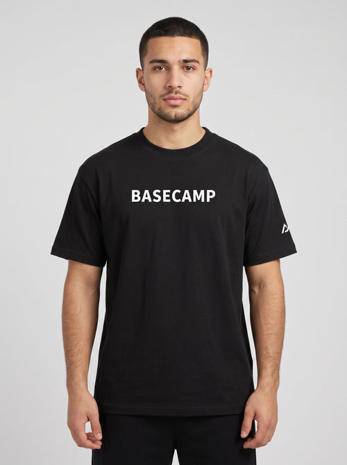 Model wearing the black BASECAMP Heavyweight Tee, front view, BASECAMP wordmark across the chest and the two-peak mark on the sleeve